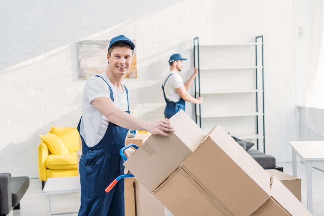 two-movers-in-uniform-transporting-cardboard-boxes-and-furniture-in-apartment.jpg