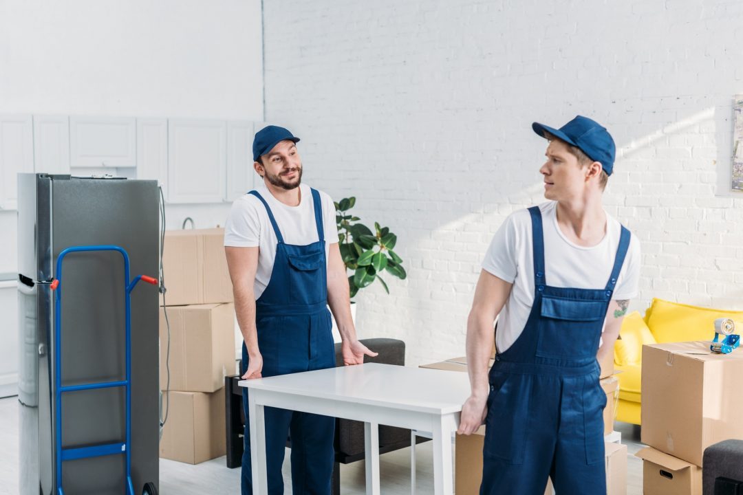 two-movers-in-uniform-transporting-table-in-apartment.jpg
